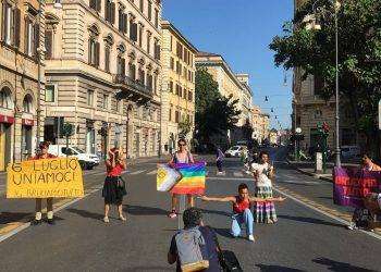 Attivistə in cerchio con tamburelli e bandiera queer danzano in ricordo dei Moti di Stonewall